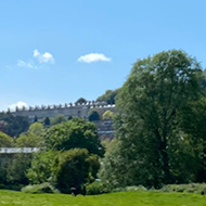 A circular hole in a rock slab, showing a view of a field, trees, houses and a clear sky behind