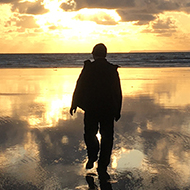Man walking towards sunset on beach