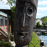 A carved wooden statue overlooks the Wallbridge Upper Lock outside the Lock Keepers Cafe, Stroud. The statue is in the foreground, and the canal and lock recede into the distance.