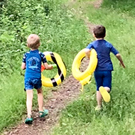 Three children running along a forest road with swimming toys.