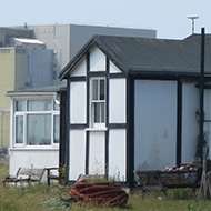 We see the surreal landscape of a Dungeness wooden cabin framed by the nuclear power station