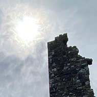 The ruins of Corfe Castle, with the sun breaking through clouds in the background