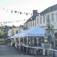 A quiet town street with stalls being set up, bunting overhead and and sunshine making things look cherry and colourful.