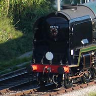 Steam train Eddystone pulls out of Corfe Castle station on the Swanage line. The view is from the castle, and shows the signal box and semaphore signals as well as the 1946 Southern Railway rebuilt West Country Class Bulleid Pacific No. 34028 ‘Eddystone’. The engine and tender are in green with glittering brass highlights.