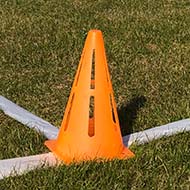 Seven ultimate frisbee players wearing white tops run across a green field under a blue sky, with the opposition in red in the background, and the pitch lines and an orange corner cone in the foreground.