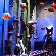 The set of the Hogwarts Great Hall from the Harry Potter Series of films, looking back from the teachers' table, with one long table against each side wall, staged ready for a Hallowe'en feast, with dozens of pumpkins suspended from the ceiling.