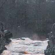 Cloudy sky, rocks, and water running towards a fall.