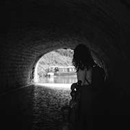A woman looking towards the end of a dark canal tunnel.