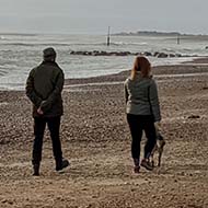 Two people walking along an empty beach together but socially distanced.