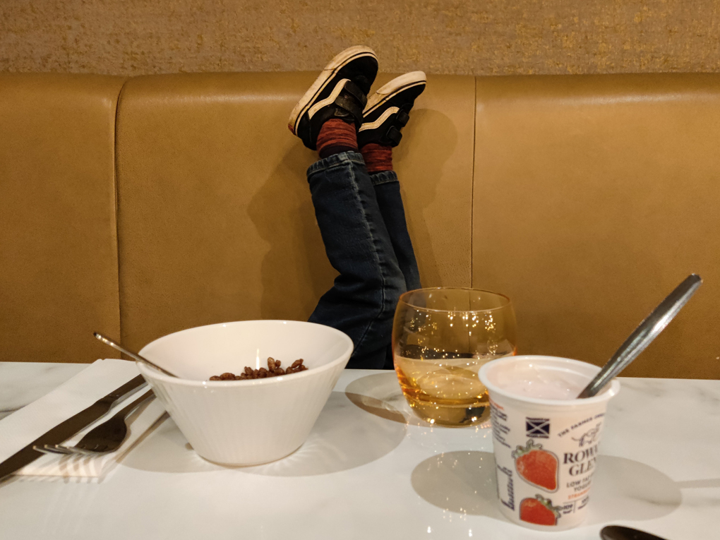 A boy's feet waving in the air at a hotel breakfast table, on which a mirror and razor lay crossed.