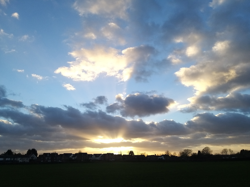 The setting sun shooting rays of light up across the blue sky