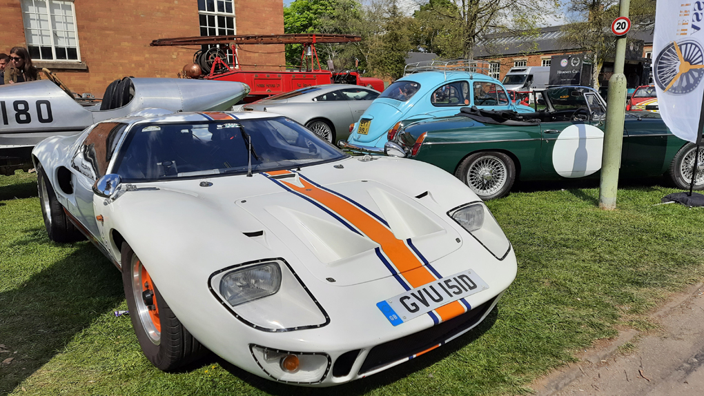 A Ford GT40 at a car show. The car is low with beuatiful curves, bright white paint, and orange and blue racing lines down the length of the car.