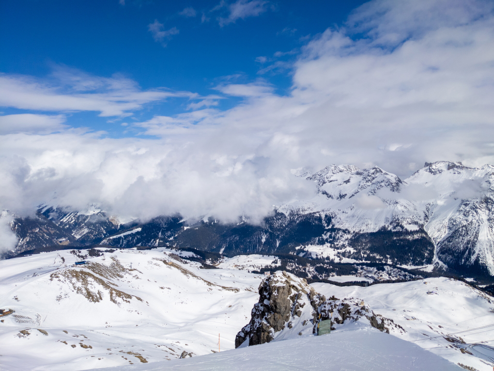 A view of brilliant white snowy mountains in bright sunshine, with blue cloudy skies above