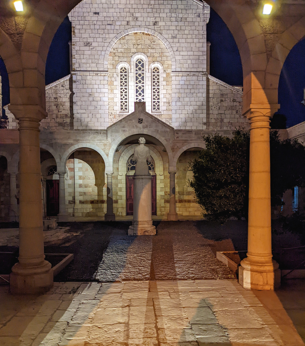 Stone statue of St Etienne at night, lit up, in stone courtyard