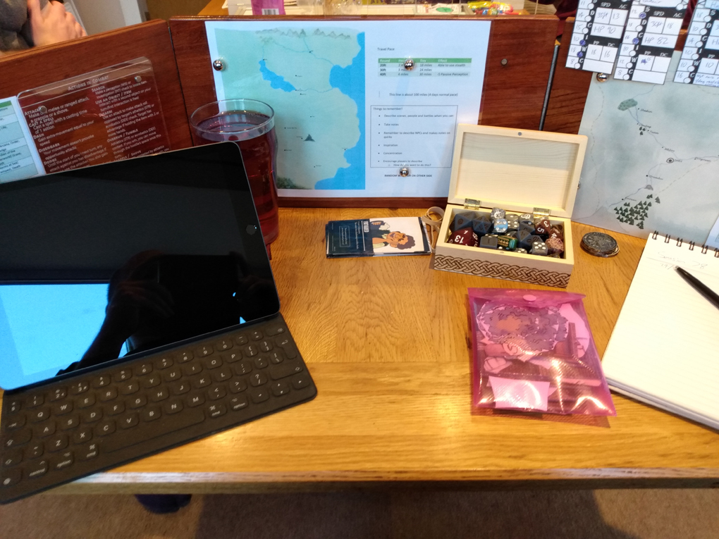 The back of a wooden dungeon master's screen that has a map affixed to the center. An iPad and dice sit behind the screen