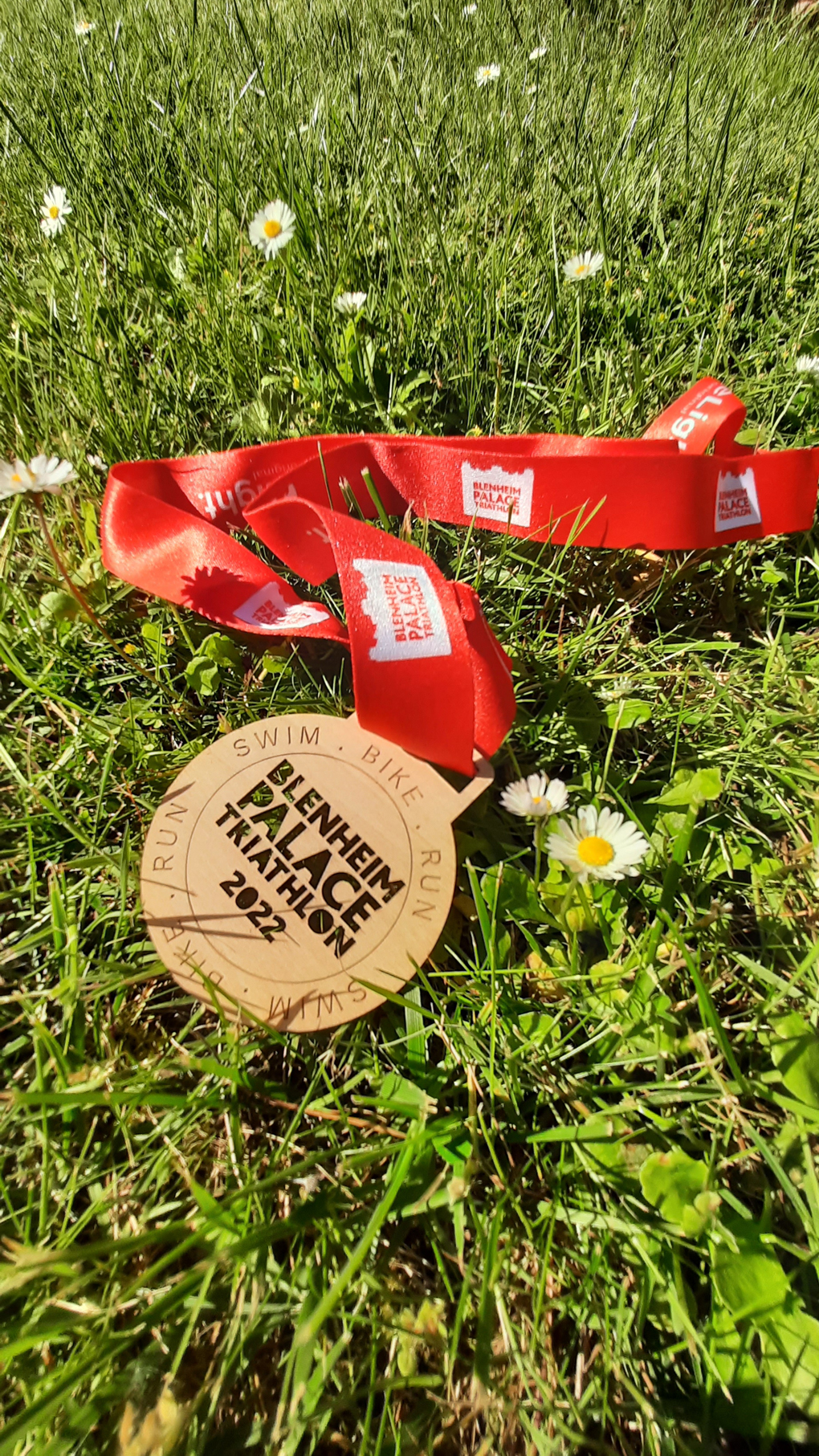 A wooden medal etched with Blenheim Palace Triathlon 2022 with a red ribbon woven around it.