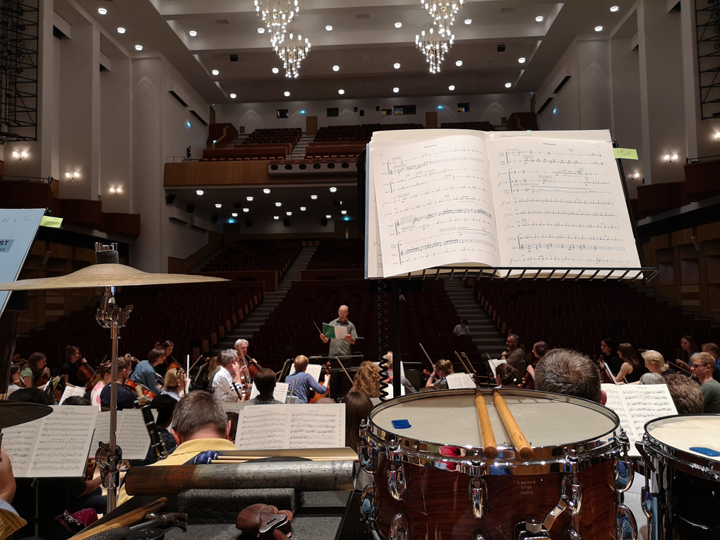 A view from the back of the orchestra showing snare drum and music stands.