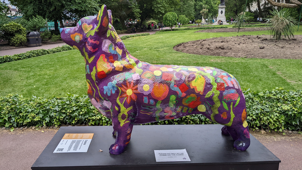 A large brightly painted statue of a corgi in a London garden.