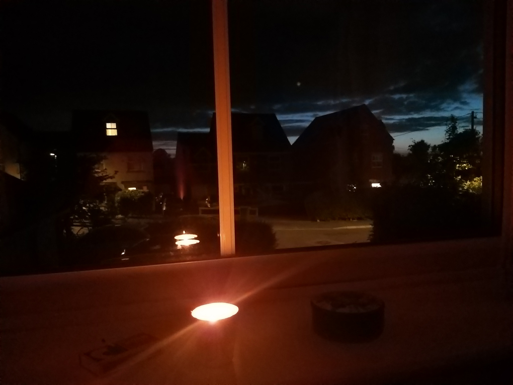 Lit tea light on a windowsill against a twilight sky