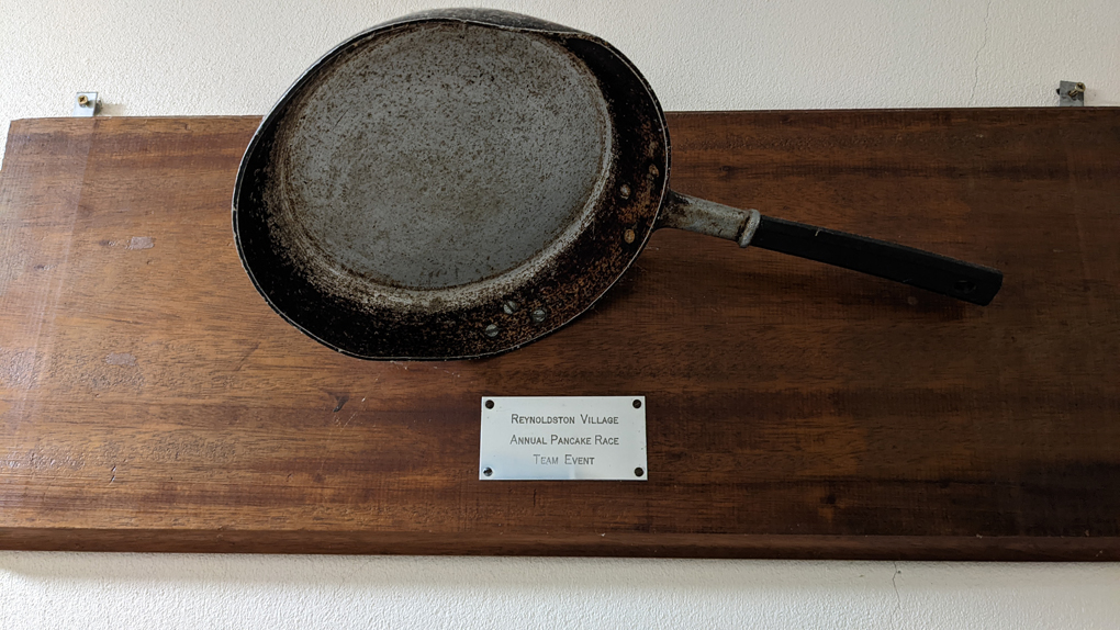 A frying pan mounted on a wooden stand with a metal plaque underneath which says 