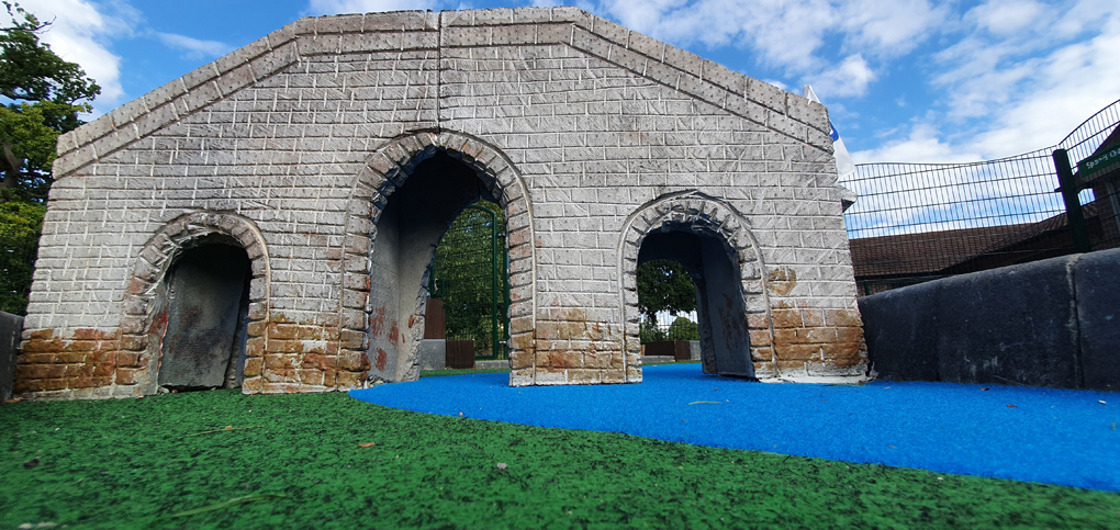 A grey bridge goes over a fake blue river on a crazy golf course.