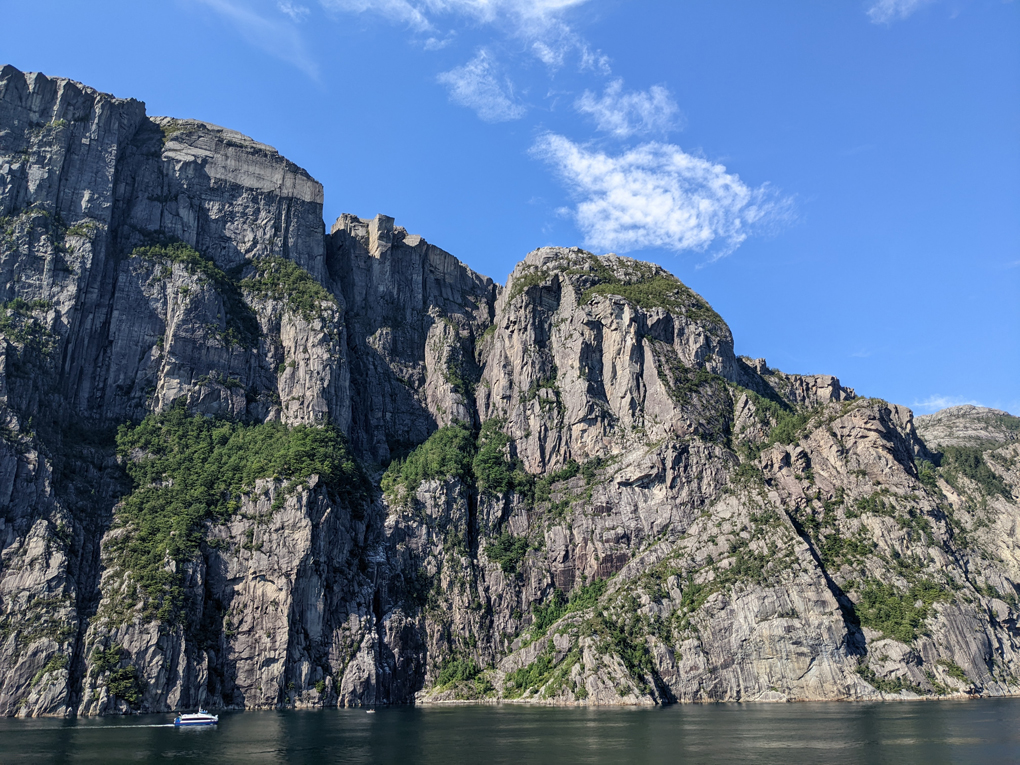 Norwegian fjord giant cliffs descending into still waters pulpit rock overhanging the top two boats at the bottom on a sunny blue sky day