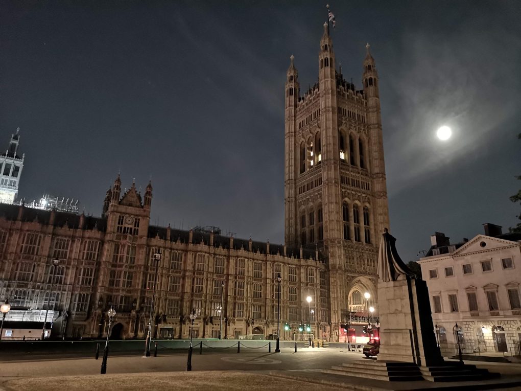 The moon shining behind the Palace of Westminster at night.