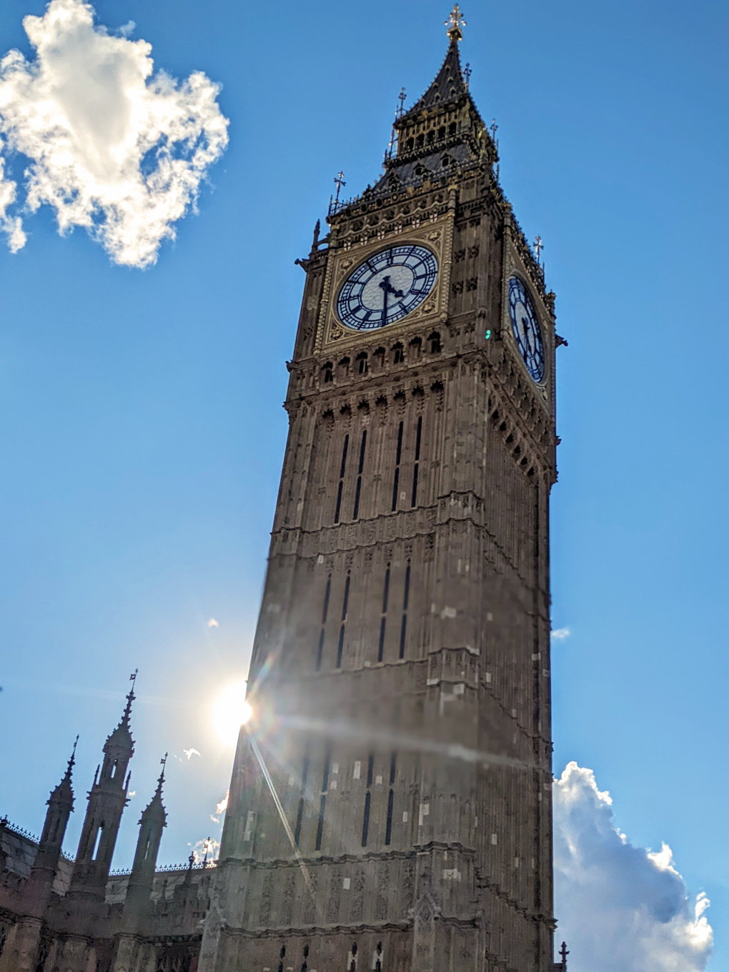 sun behind clock tower, blue sky with clouds