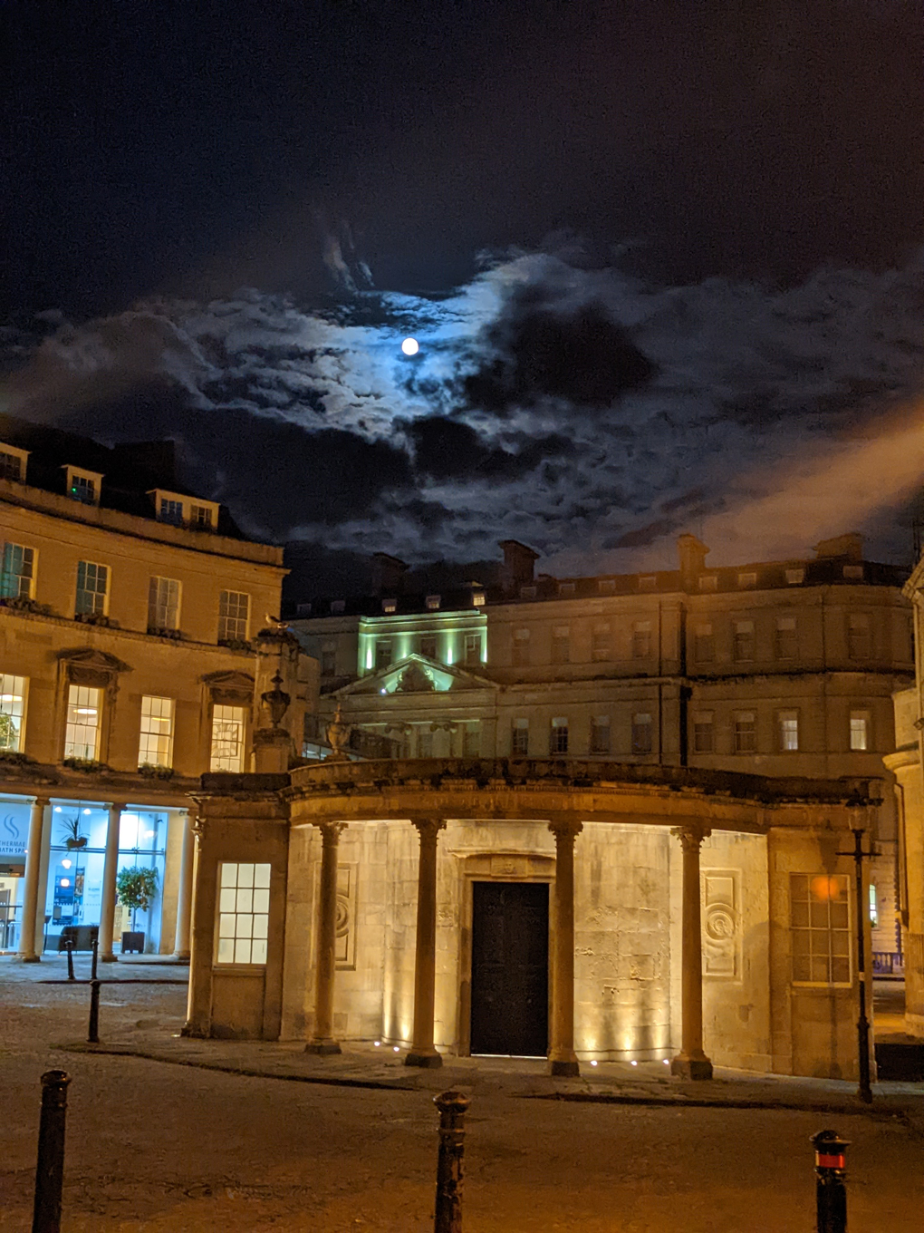 Cross baths lit up at night with moon shining between clouds above