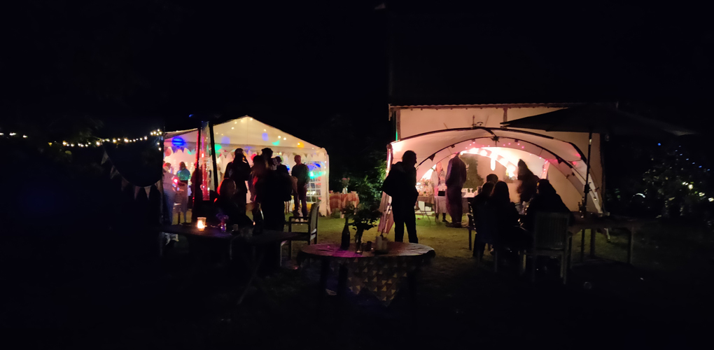 In pitch black night people are silhouetted against the colourful lights from party tents