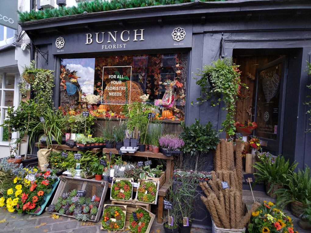 A lovely florist shop front with a beautiful autumnal display in the window and lots of bright orange and yellow flowers and green foliage underneath