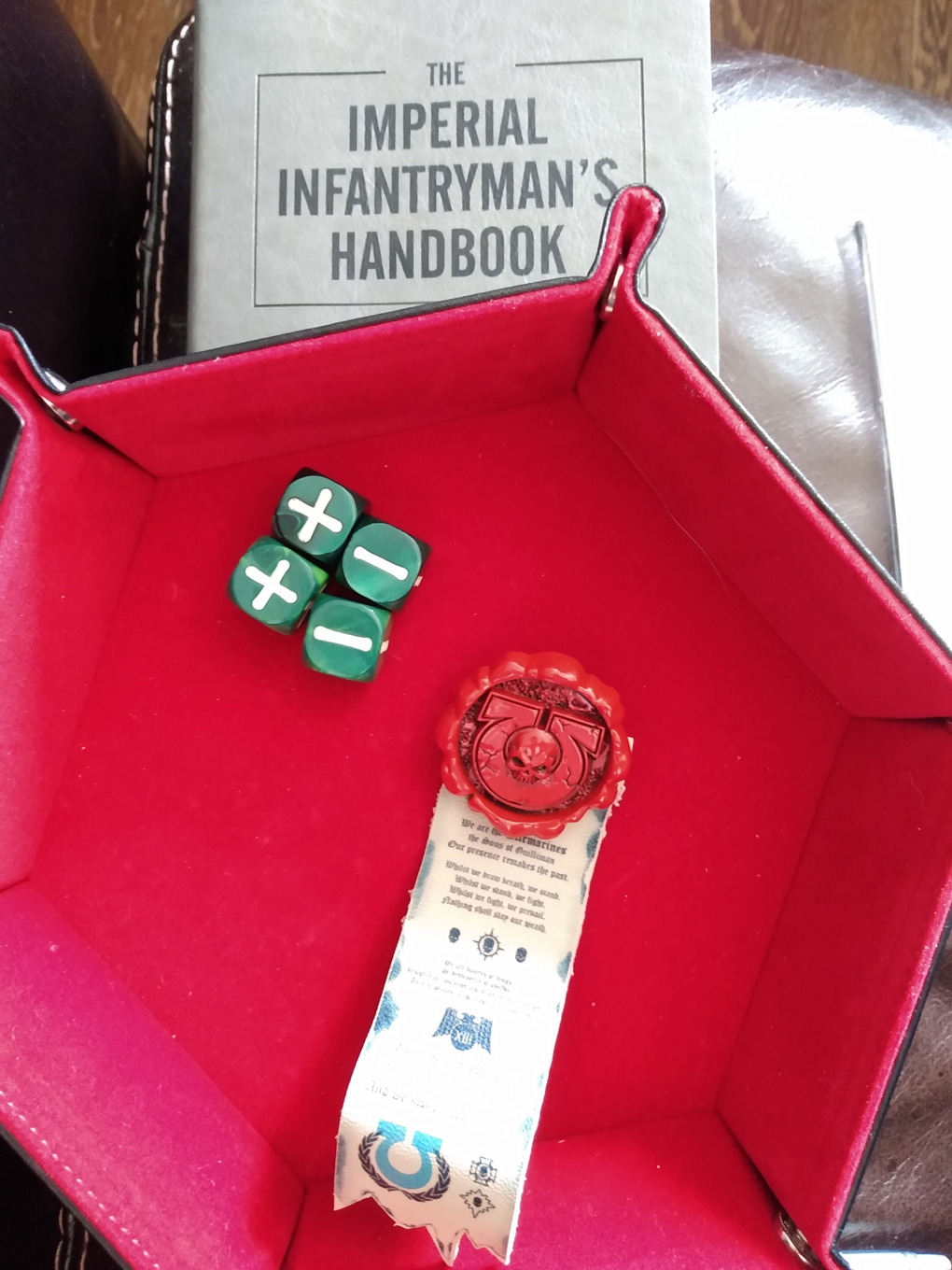 A red felt-lined dice tray holds four dice and a novelty purity seal from warhammer 40,000
