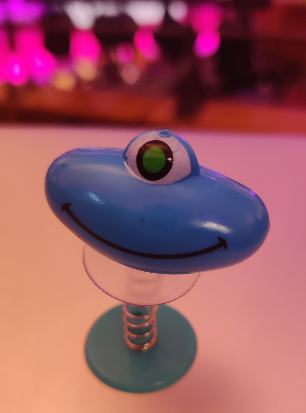 A blue one-eyed alien on a spring on a table in a conference theatre
