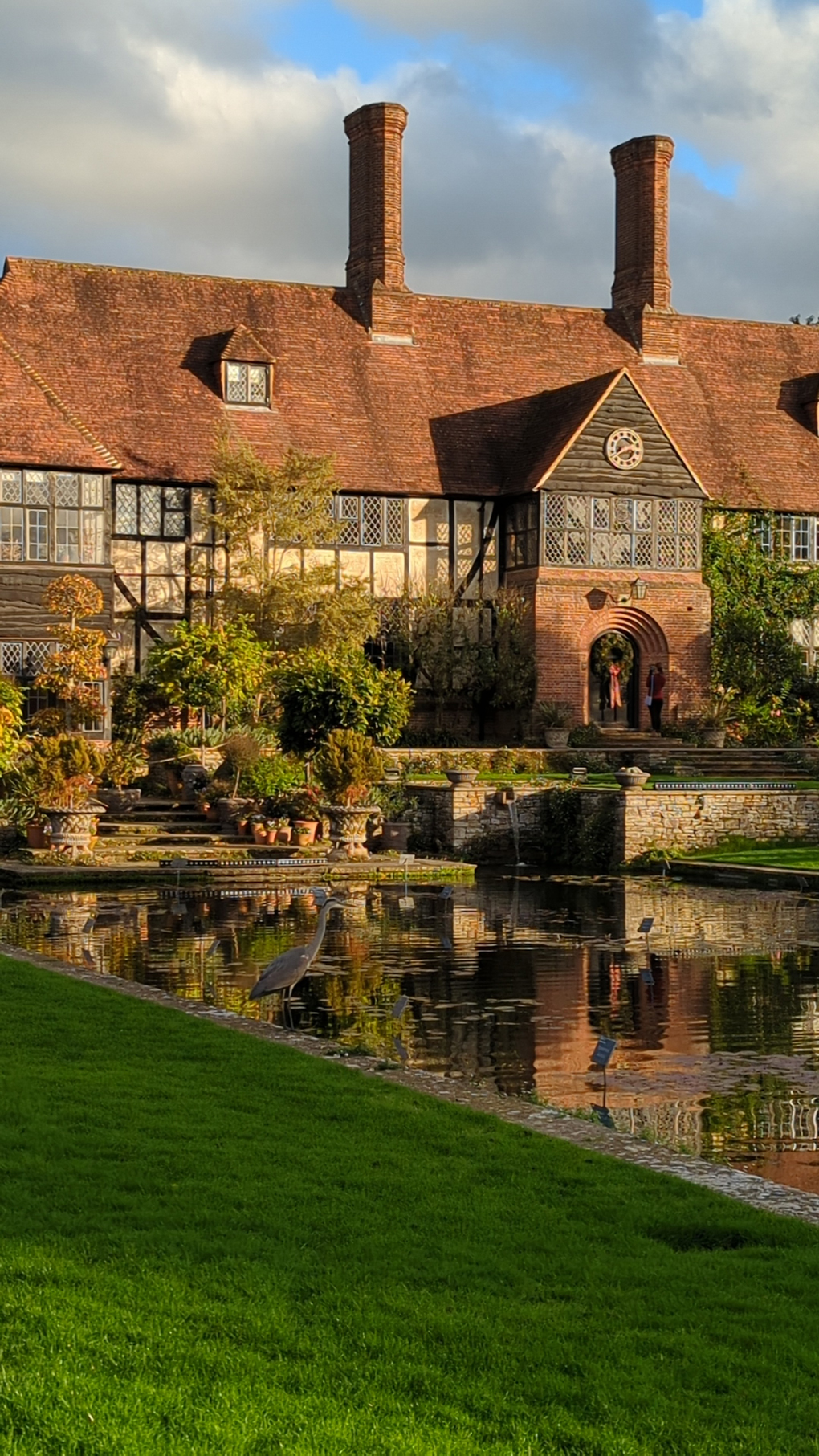 Photo of RHS Wisley late afternoon as the sun is setting lighting up The Laboratory building at RHS Wisley overlooking the ornamental pond which is reflecting the Arts and Craft style building