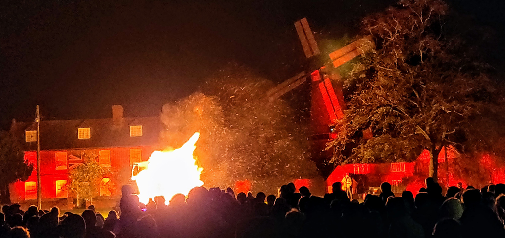 Picture of a bonfire in the left of the photo and windmill in orange in the background.