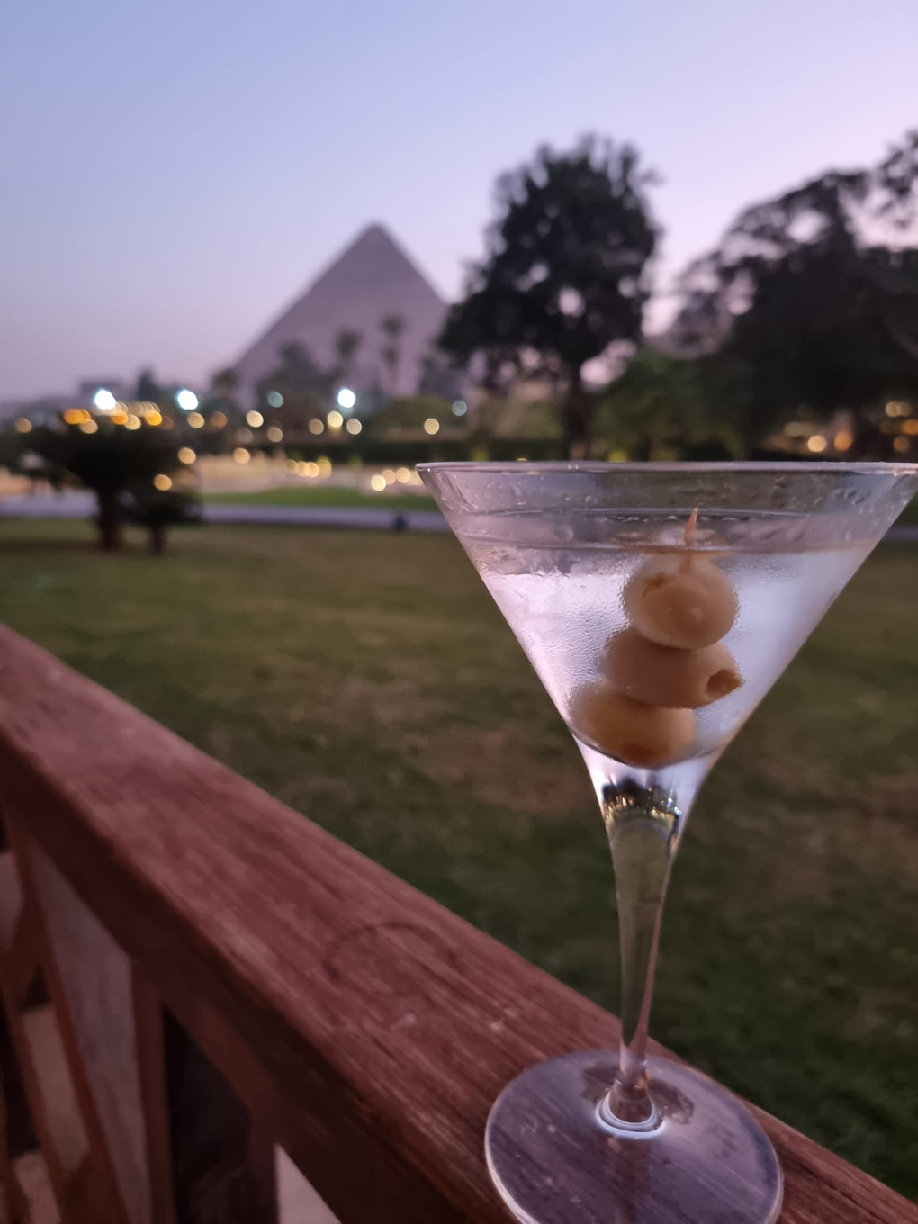 A martini sitting on the arm of a chair with a pyramid in the background