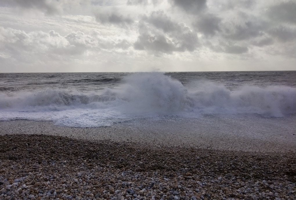 Big waves crashing into a pebbly beach throwing up large clouds of spray