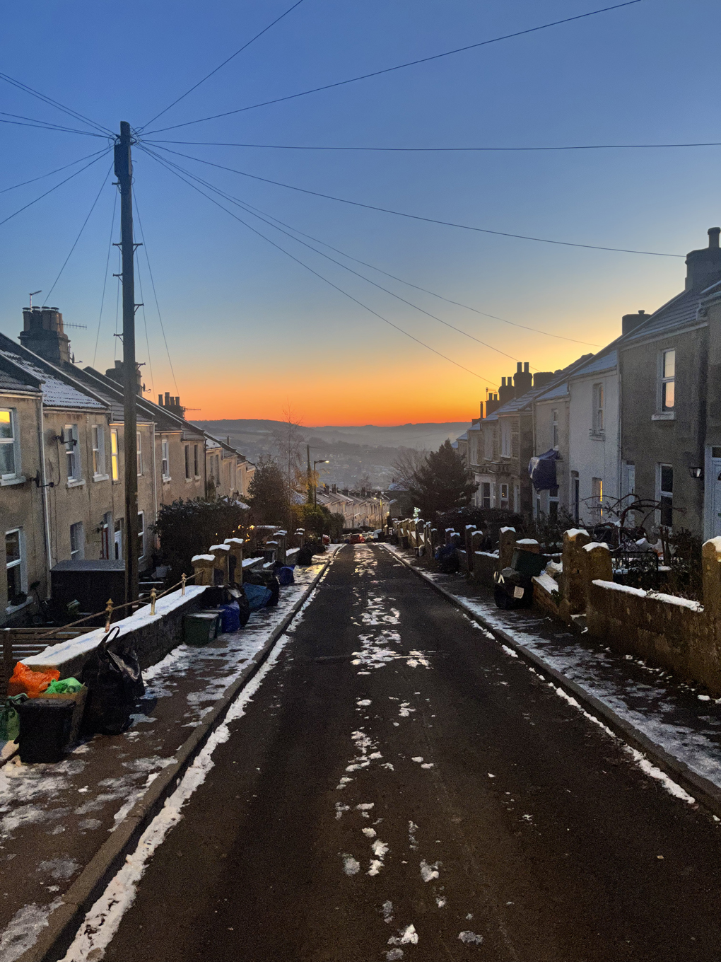 Looking down a steep icy street lined with houses towards a bright, multicoloured sunrise