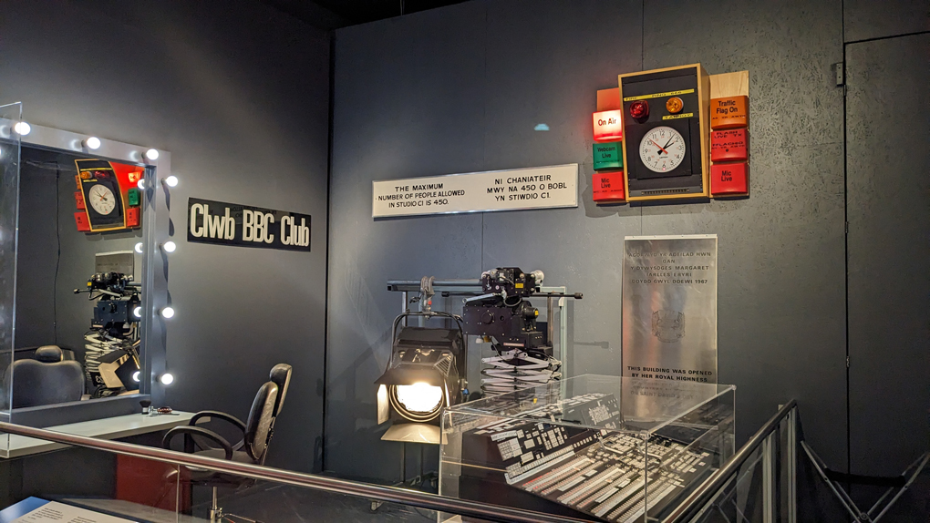 A radio studio clock and on-air light, a television mixing desk, chairs, dressing room mirrors and various pieces of signage - All on display in a museum.