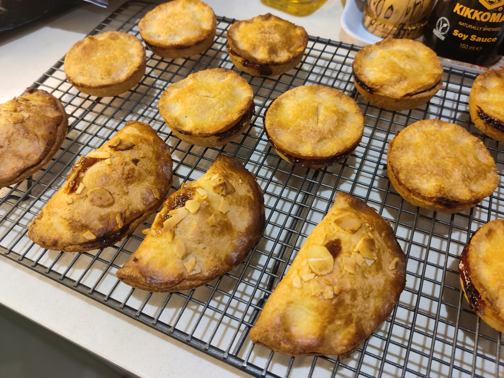 A mixture of normal round mince pies and Cornish pasty shaped ones are cooling on a wire rack