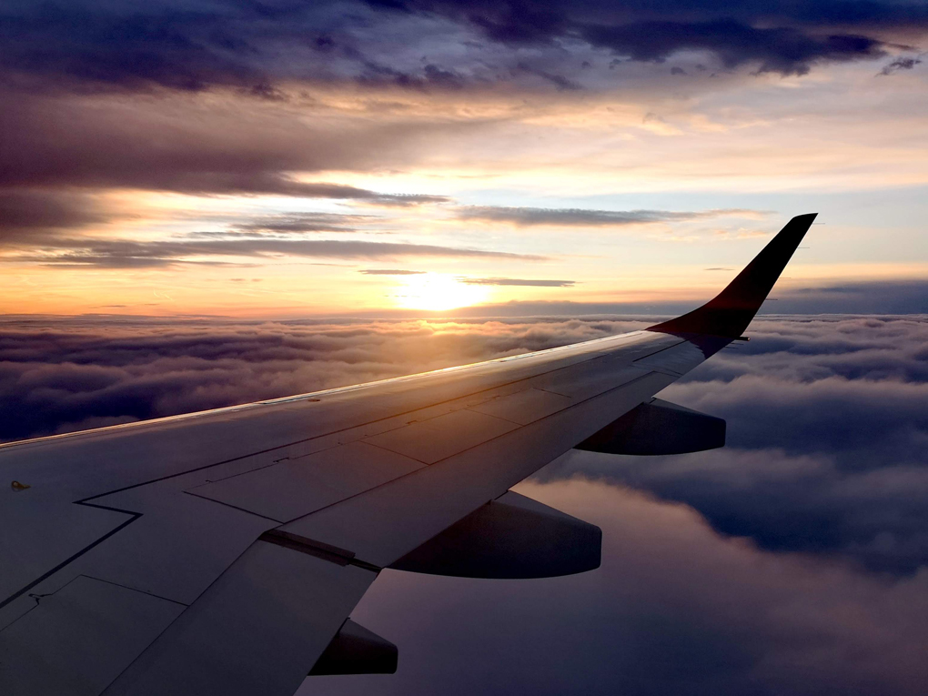 View out the window over an aeroplane wing with a sunset and clouds.