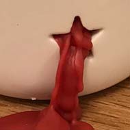 Red candle wax squeezing through a star shaped hole in a lantern.