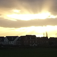 The setting sun shooting rays of light up across the blue sky