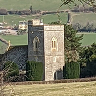 Picture of a quaint church through the frame of a gate and overarching tree.