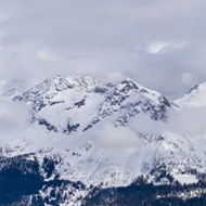 A view of brilliant white snowy mountains in bright sunshine, with blue cloudy skies above