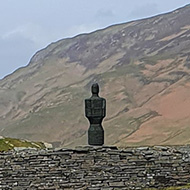 In the middle distance a slate statue sits on a slate wall, at the foot of a mountain. In the distance mountains