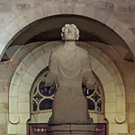 Stone statue of St Etienne at night, lit up, in stone courtyard