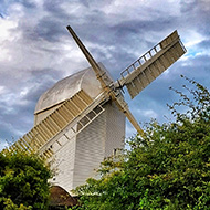 Windmill behind green hedge with blue sky and clouds