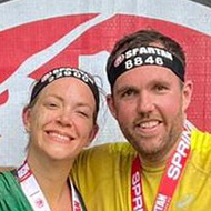 Two people standing in front of a logo celebrating completing the race