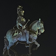 A statue of a man riding a horse is lit up from below with multicoloured lights